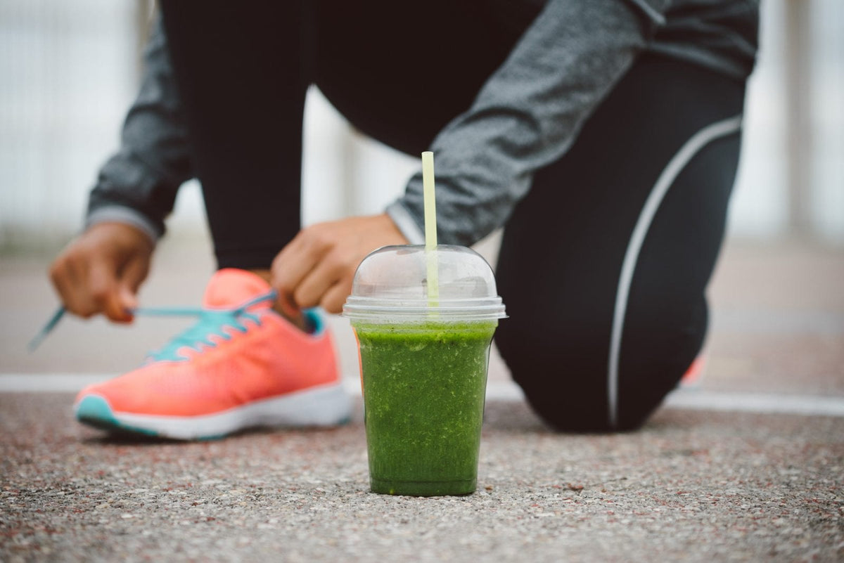 EIne Frau schnürt sich die Sportschuhe. Vor ihr ein grüner Smoothie