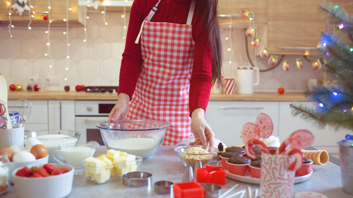 Eine Frau in rotkarierter Küchenschürze steht in einer Küche mit Weihnachtsdekoration und backt.