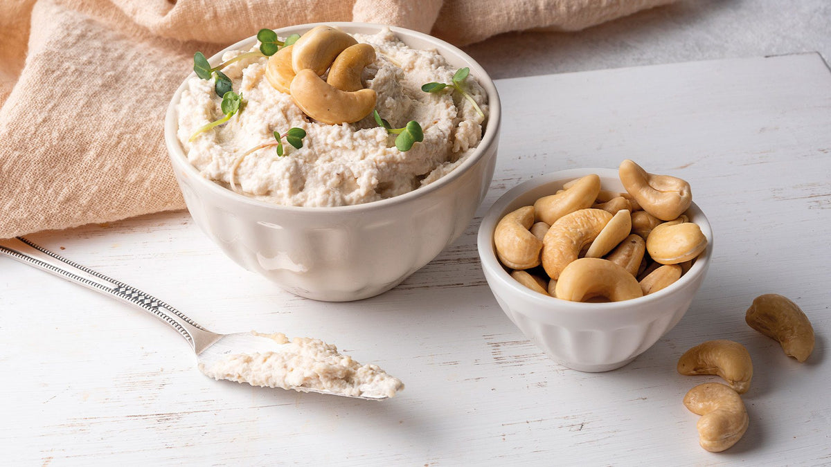 Eine weiße Schüssel mit cremigem Cashew-Dip und eine kleinere weiße Schüssel mit Cashew-Kernen.