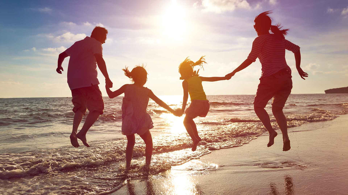Eine vierköpfige Familie ist am Strand und macht einen Luftsprung