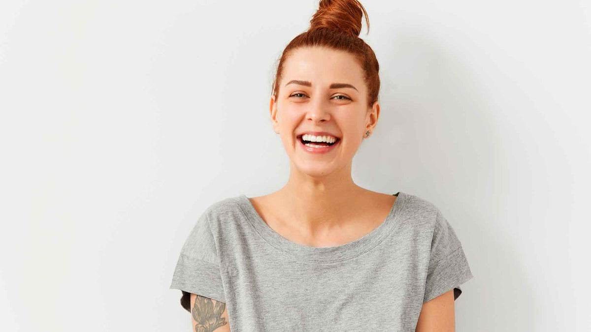Eine lachende, junge Frau in grauem T-Shirt und hochgesteckter
Frisur.