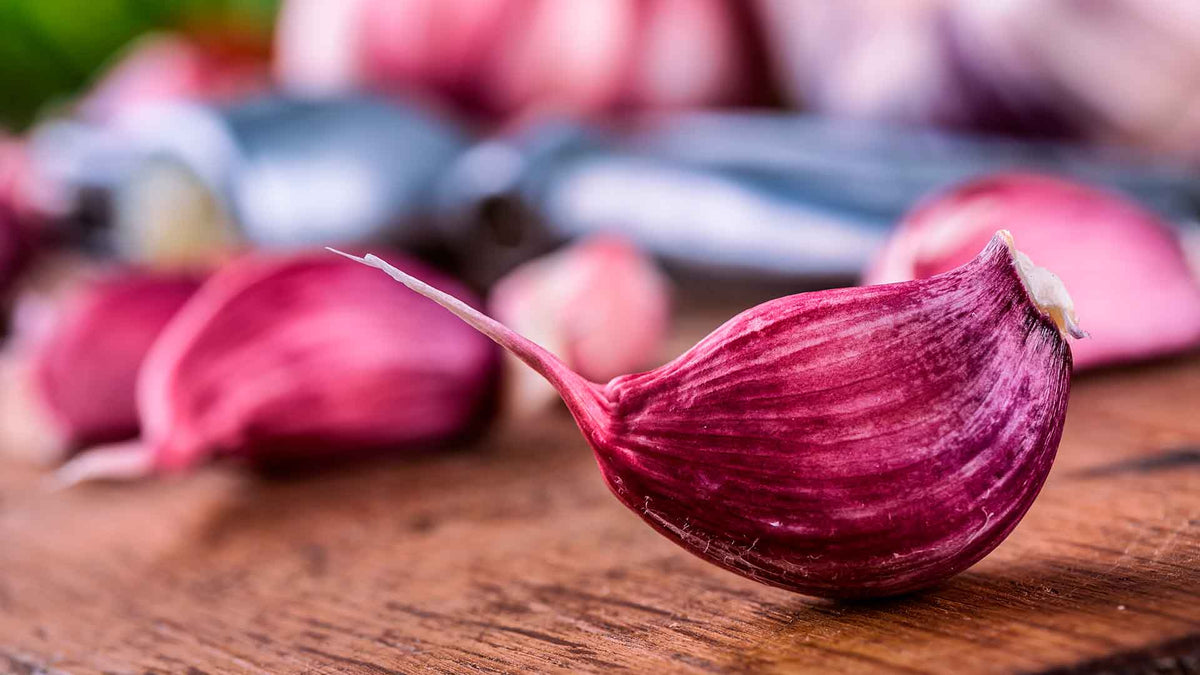 Nahaufnahme: Mehrere rote Knoblauchzehen auf einem Holzuntergrund