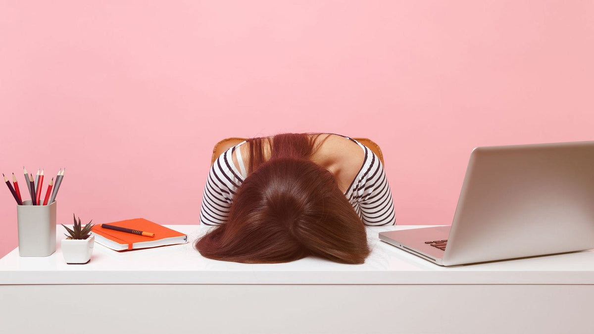 Eine Frau hat vor lauter Stress den Kopf auf den Schreibtisch gelegt