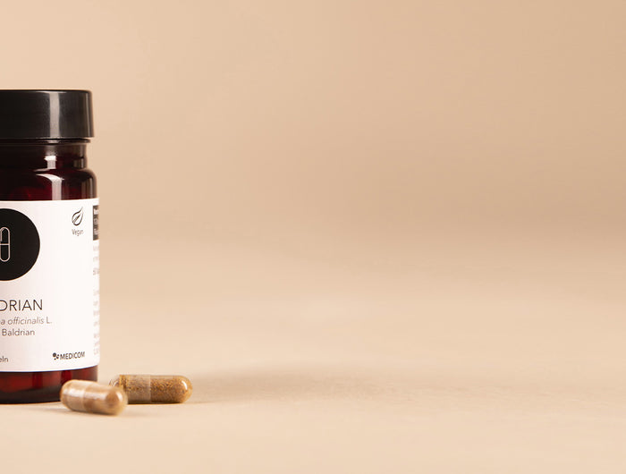 Die Produktdose von Baldrian-Kapseln von Medicom mit zwei Kapseln im Vordergrund