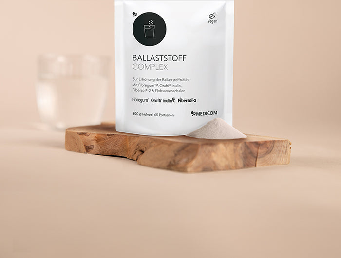 Der Zippbeutel von Ballaststoffpulver und ein Haufen Ballaststoffpulver vor der Packung. Alles auf einem Holztablett.