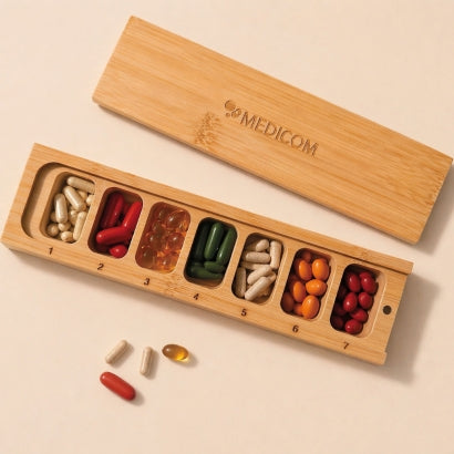 Die Medicom Kapselbox aus Bambusholz, mit sieben durchnummerierten Fächern. Die Kapselbox von oben aufgenommen und befüllt mit bunten Kapseln. Vier Kapseln im Vordergrund
