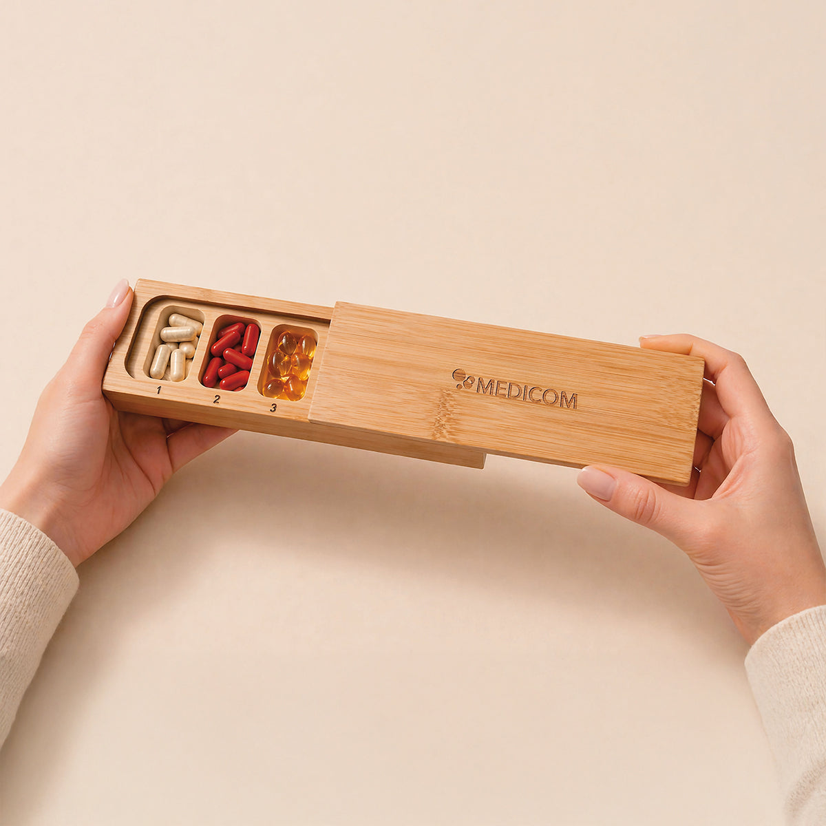 Hände, die eine „Medicom Kapselbox“ von Medicom halten, einen Tablettenbehälter aus Holz mit drei Fächern, in denen verschiedene Tabletten und Kapseln aufbewahrt werden.