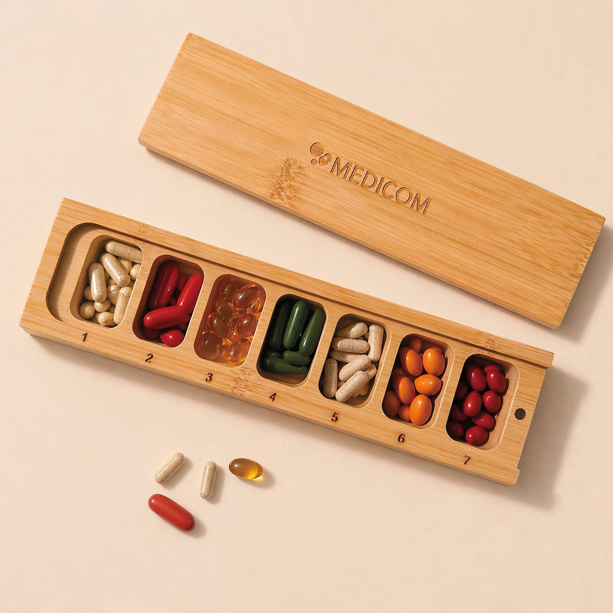 Die „Medicom Kapselbox“ von Medicom ist ein Tablettenbehälter aus Holz mit sieben Fächern, die jeweils mit verschiedenfarbigen Kapseln und Tabletten gefüllt sind.