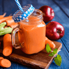 Karotten-Smoothie mit Karotten und Äpfeln im Hintergrund