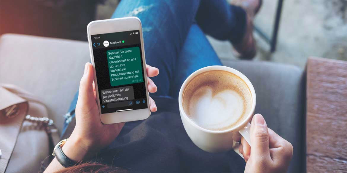 Person, die ein Smartphone mit einer deutschen Textnachricht in der Hand hält und mit einer Kaffeetasse auf einem Tisch sitzt.
