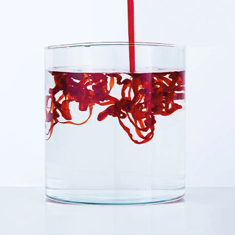Rote Flüssigkeit wird in ein Glas mit klarem Wasser gegossen und wirbelt in komplizierten Mustern.