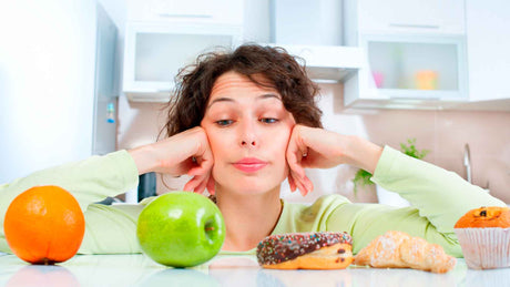 Eine Frau hat vor sich eine Orange, einen grünen Apfel  und Gebäck wie Donuts liegen