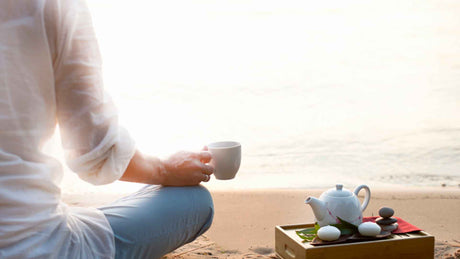 Eine Frau trinkt am Strand Tee mit einem Churna aus dem Ayurveda.