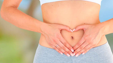 Eine Frau mit nacktem Oberbauch formt mit ihren Händen ein Herz um ihren Bauchnabel.