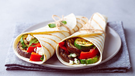 Zwei Auberginenrollen auf einem Teller. Man sieht im Wrap Auberginen, Zucchini und Paprika.