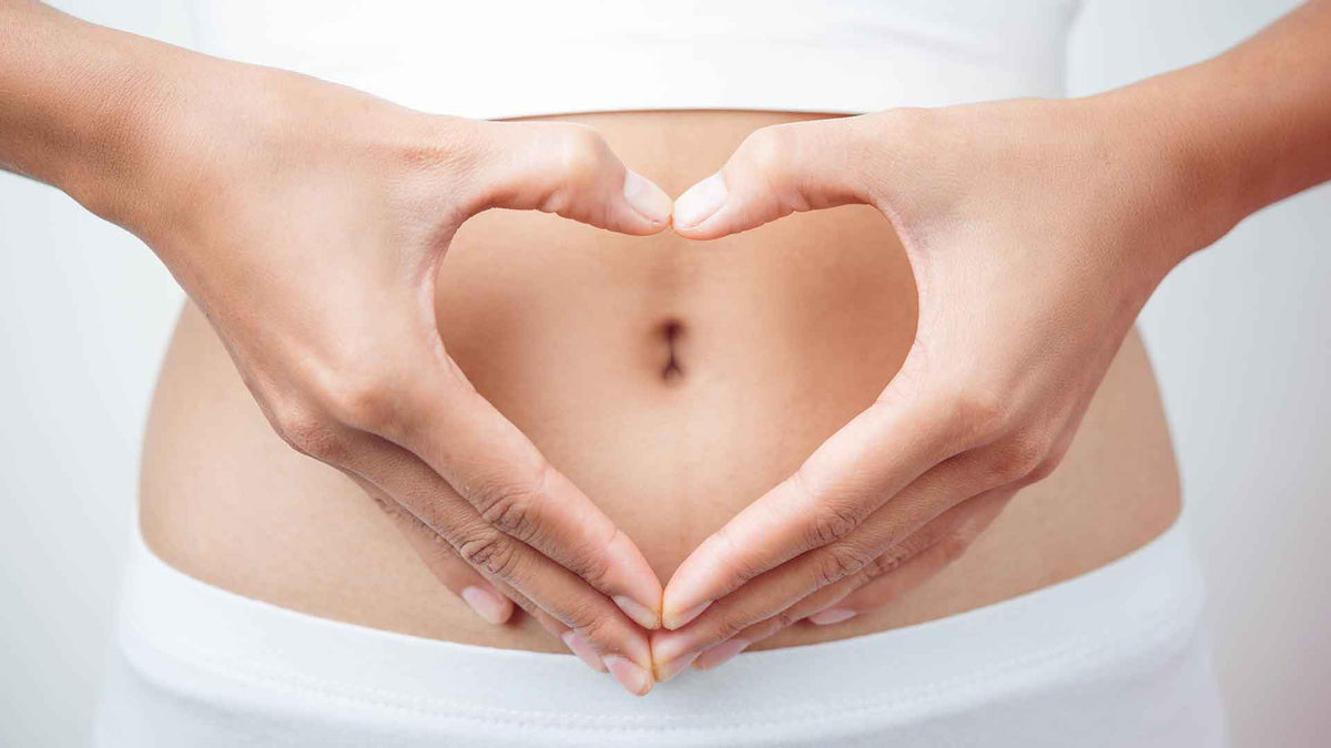 Eine Frau in weißer Unterwäsche formt mit den Händen ein Herz um den Bauchnabel herum.