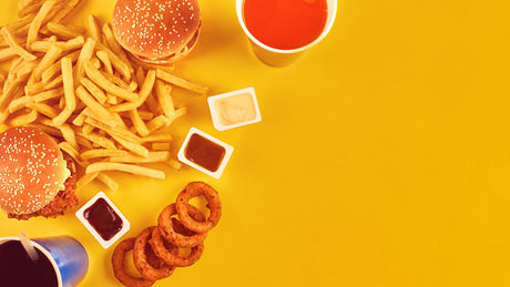 Fast Food wie Hamburger, Pommes Frites und Frittiertes auf gelbem Hintergrund