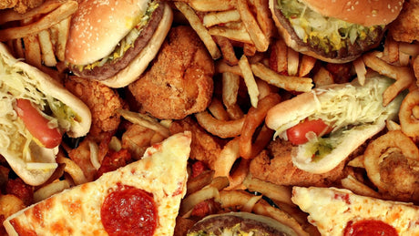 Nahaufnahme von verschiedenen Sorten Fast Food wie Hamburger, Hot Dogs, Pommes Frites, paniertes Essen, Pizza-Käse-Salami etc.
