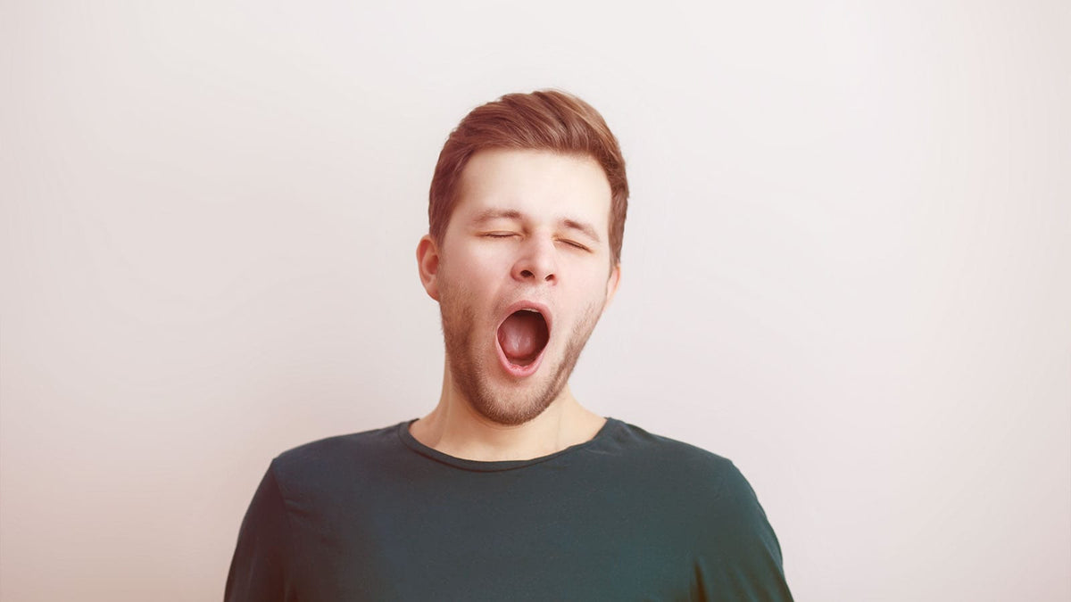 Ein junger Mann in dunkelgrauem T-Shirt gähnt genüsslich und hat die Augen dabei geschlossen.