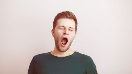 Ein junger Mann in dunkelgrauem T-Shirt gähnt genüsslich und hat die Augen dabei geschlossen.