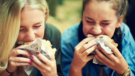 Zwei junge Frauen haben Heißhunger auf Hamburger und beißen herzhaft rein.