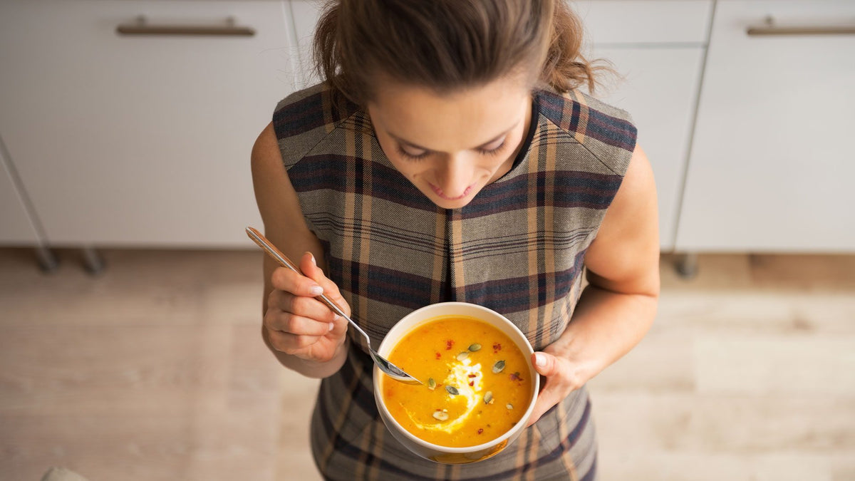 Ansicht von oben auf eine Frau, die eine Schüssel mit Kürbissuppe in der Hand hält.