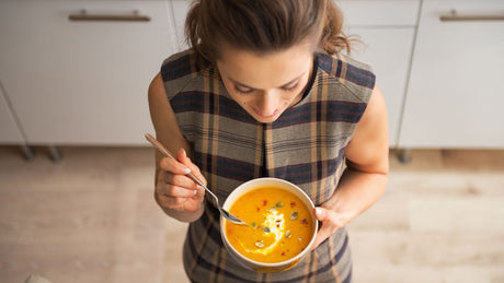 Ansicht von oben auf eine Frau, die eine Schüssel mit Kürbissuppe in der Hand hält.