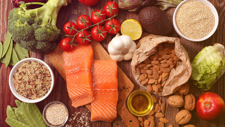 Gesundes Essen wie Lachsfilets, Gemüse, Obst, Naturreis, Haferflocken auf einer Holzunterlage.