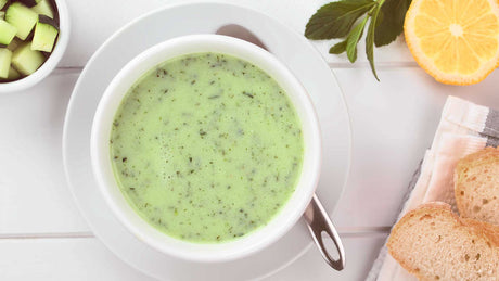 Grüne Gurkensuppe in einer weißen Schale mit Joghurt, Gurkenstückchen, Zitrone und zwei Scheiben Weißbrot