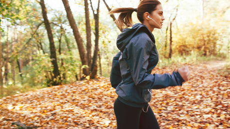 Eine junge Joggerin läuft durch einen Wald mit Herbstblättern auf dem Boden.