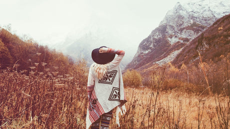 Eine Frau steht vor einer Berglandschaft. Es ist neblig und kalt.