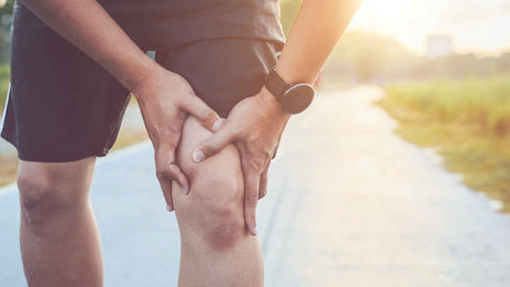 Ein Mann in Sportbekleidung fasst sich an sein linkes Knie
