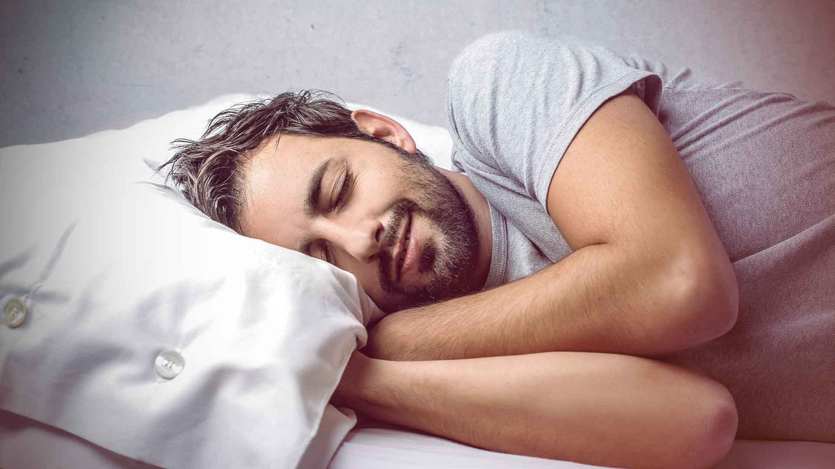 Ein Mann in grauem T-Shirt schläft seitlings auf einem weißen Kissen.