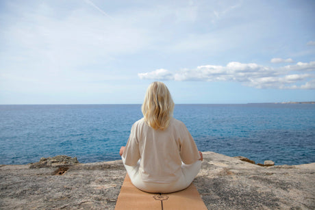 Yogalehrerin in der Meditationshaltung dem Meer zugewandt.