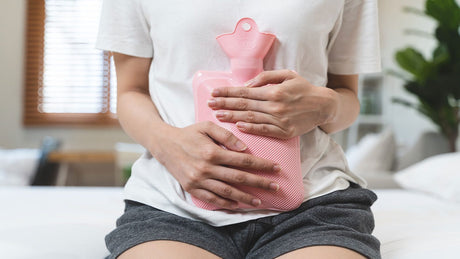 Eine Frau hält sich eine rosa Wärmflasche wegen Regelschmerzen an den Bauch