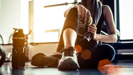 Eine Frau ruht sich nach dem Sport aus. Sie hält Obst in der Hand und neben ihr ist eine Trinkflasche
