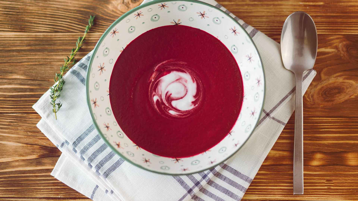 Schön angerichtete Suppe mit Roter Beete und Möhren und einem Schuss Crème fraîche zum Verfeinern. Neben der Suppenschüssel ist ein Suppenlöffel