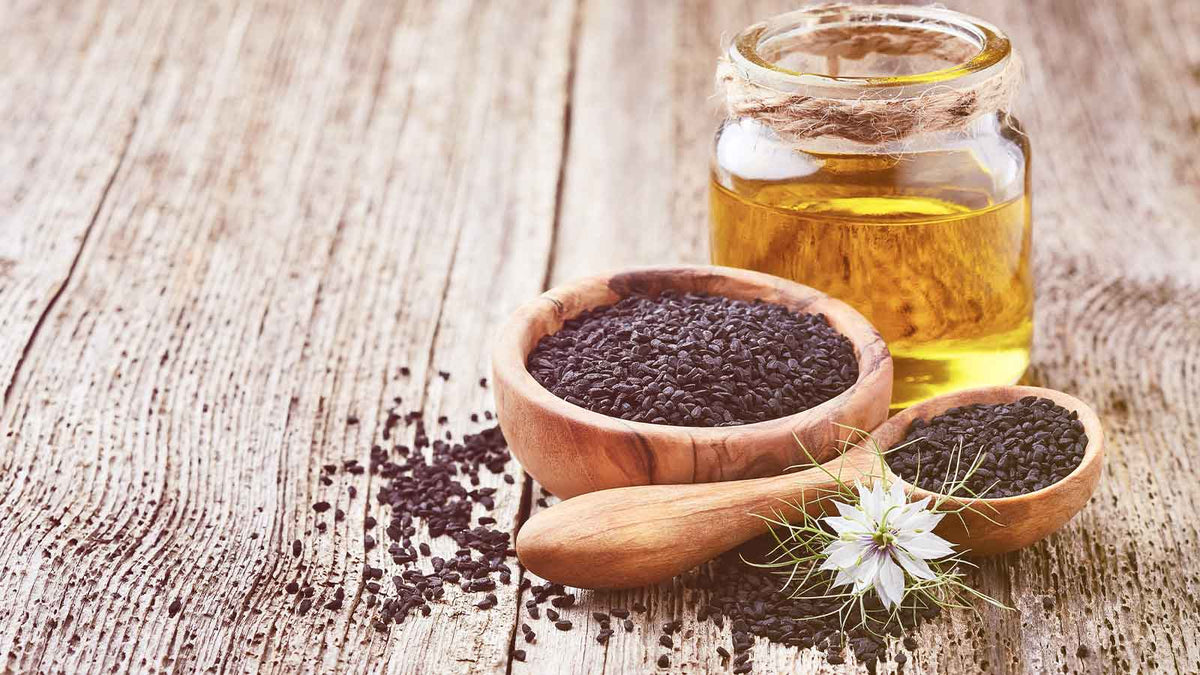 Schwarzkümmelsamen in einer Schale und gehäuft in einem Holzlöffel, eine Glasflasche mit Schwarzkümmelöl.
