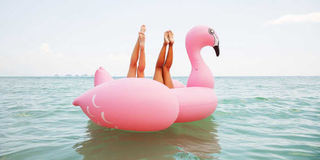 Zwei junge Frauen liegen rücklings in einer Riesen-Flamingo-Luftmatratze im Meer. Man sieht nur ihre nach oben gestreckten Beine.