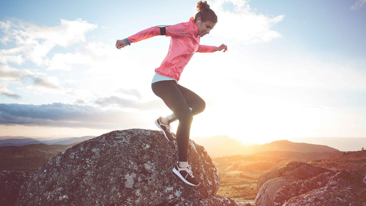 Eine junge Frau in Sportkleidung joggt durch eine Berglandschaft in der Morgensonne.