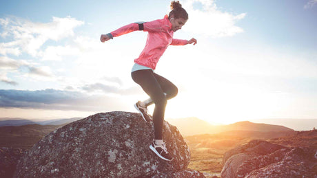 Eine junge Frau in Sportkleidung joggt durch eine Berglandschaft in der Morgensonne.