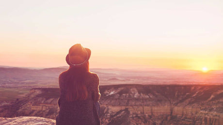 Eine Frau sitzt auf einem Hügel und schaut auf eine Landschaft mit Weitblick