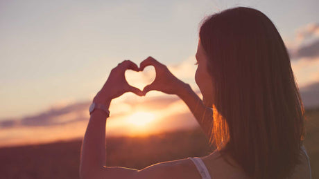 Eine Frau formt mit ihren Fingern in der Abendsonne ein Herz.