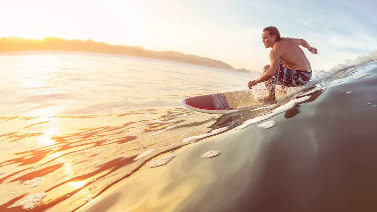 Ein junger Surfer in Badehose reitet mit einem Surfbrett auf einer Meereswelle.