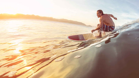 Ein junger Surfer in Badehose reitet mit einem Surfbrett auf einer Meereswelle.