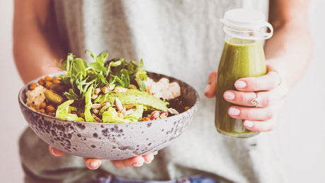 Eine Frau hält in der einen Hand eine Salatschüssel und ein Smoothie