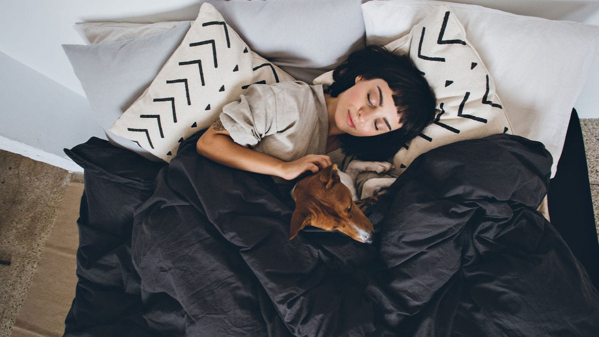 Ein junge Frau schläft mit ihrem Hund im Bett