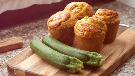 Auf einem Holzbrett liegen vier Zucchini-Muffins und zwei Zucchini