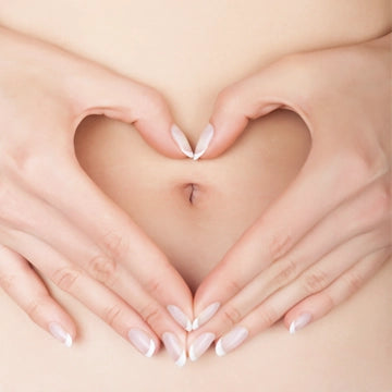 Zwei Frauenhände formen ein Herz um den Bauchnabel herum