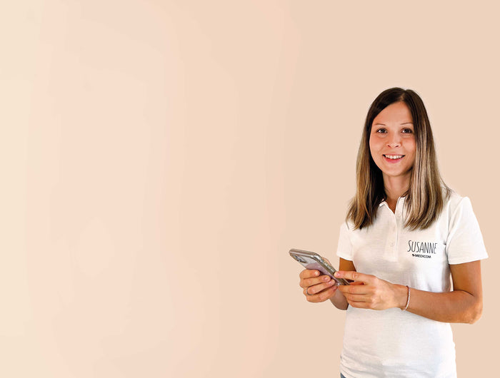 Susanne, die Vitalstoffexpertin von Medicom lächelt in die Kamera und hält ein Handy in der Hand.